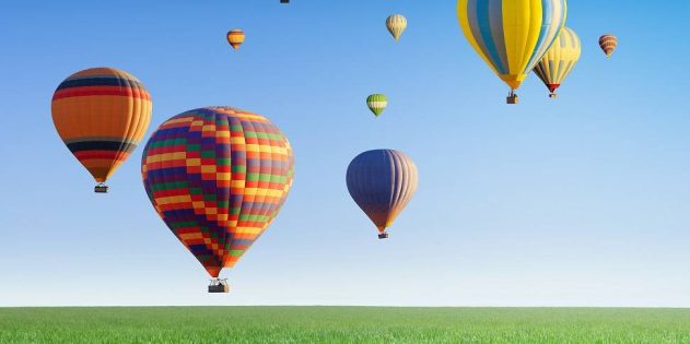 Hot air balloons flying in clear blue sky above green grass field